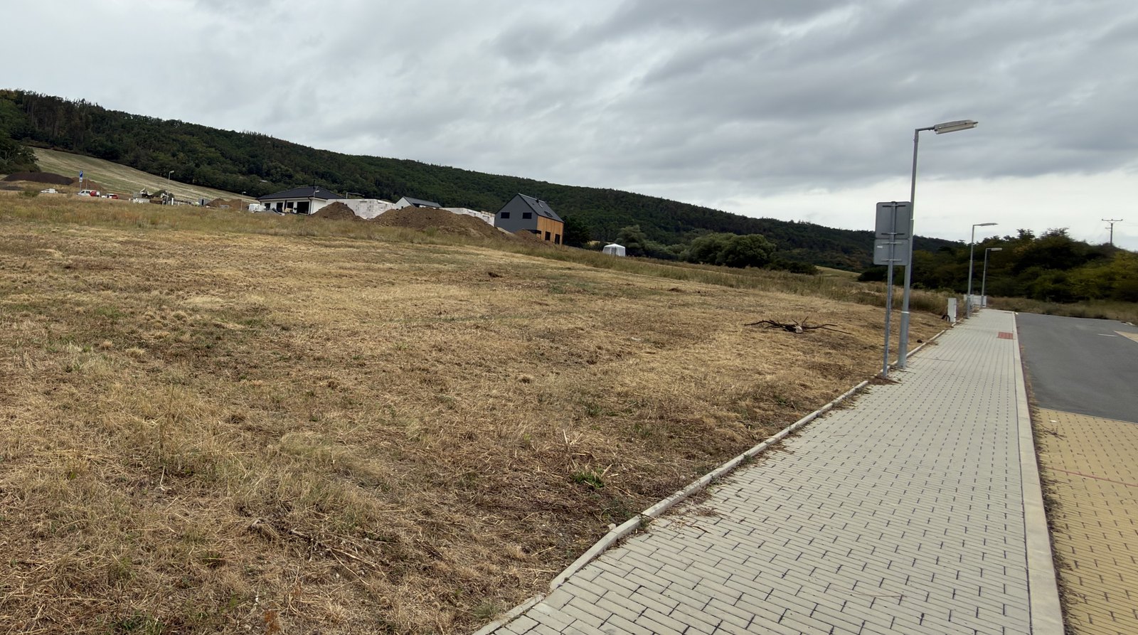 Surová fotka: prázdná parcela a chodník pod šedou oblohou